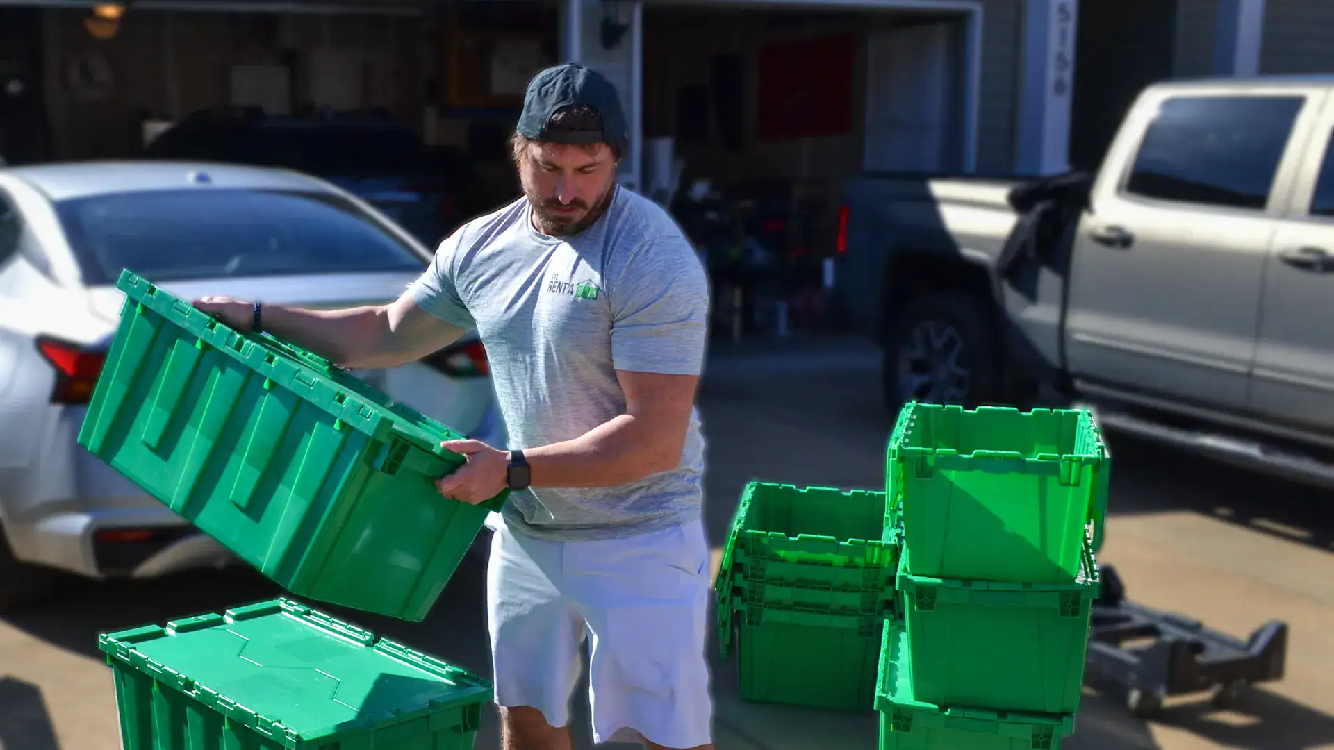 Man stacking green plastic storage bins outside.